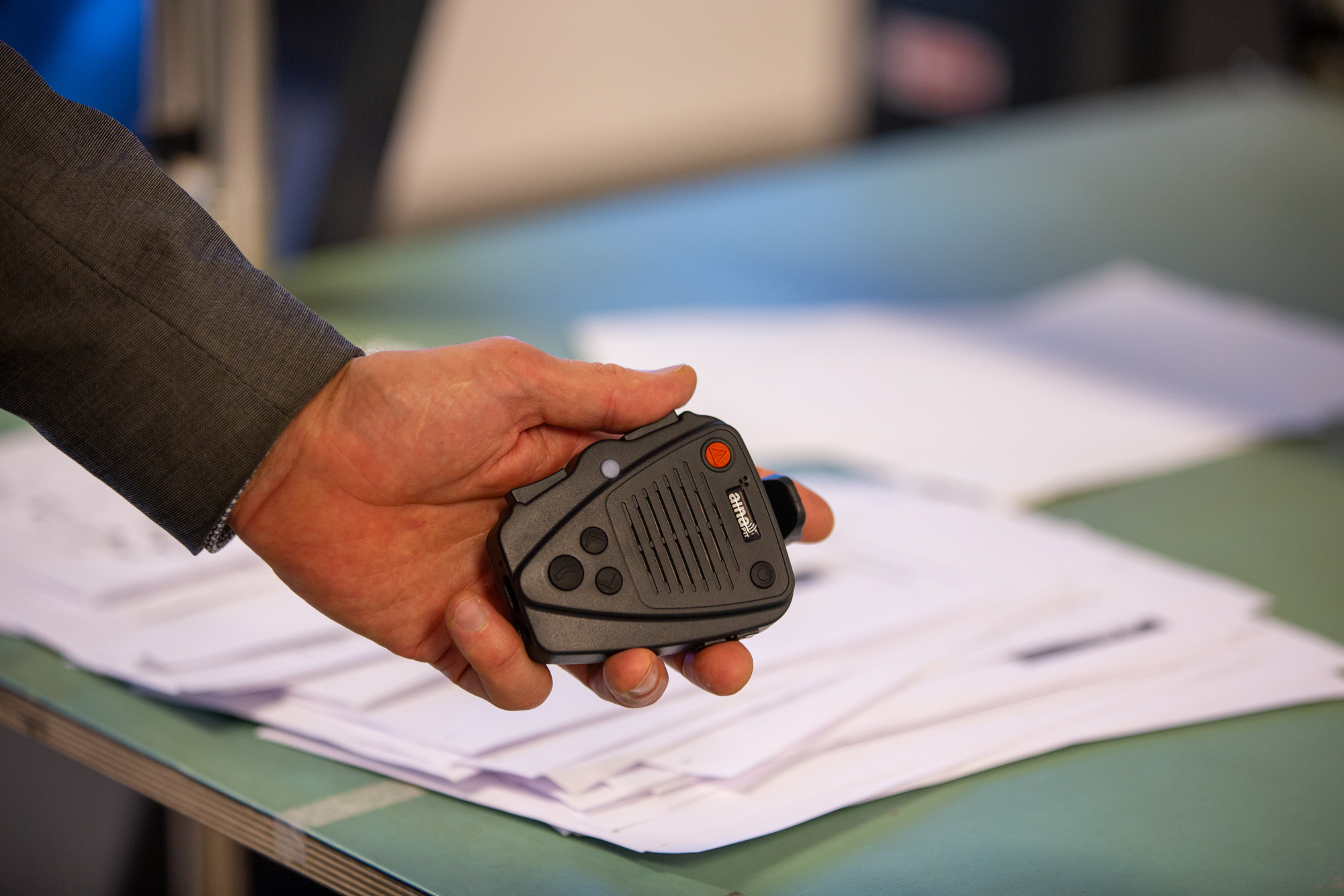 AINA PTT Voice Responder -kaiutinmikrofoni mustalla taustalla. Laite on musta, siinä näkyy painikkeita ja se on suunniteltu vaativaan kenttätyöhön.